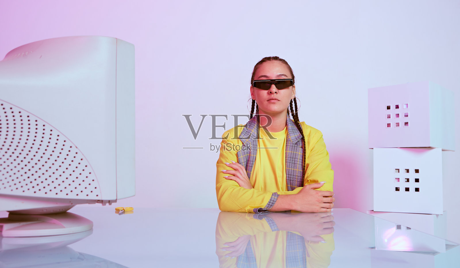 时尚的亚洲女性办公室职员戴着太阳镜坐在办公桌前的老式电脑。彩色的霓虹灯照片摄影图片