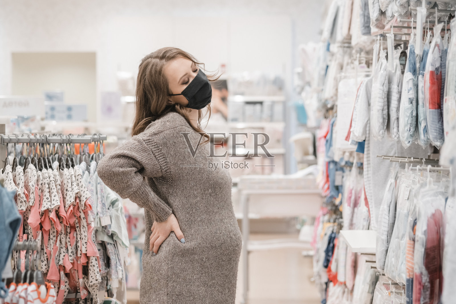 年轻美丽的孕妇在卫生口罩选择婴儿衣服，婴儿车或婴儿车的新生儿。为孕妇和婴儿购物。流行病生活方式的预防措施。照片摄影图片