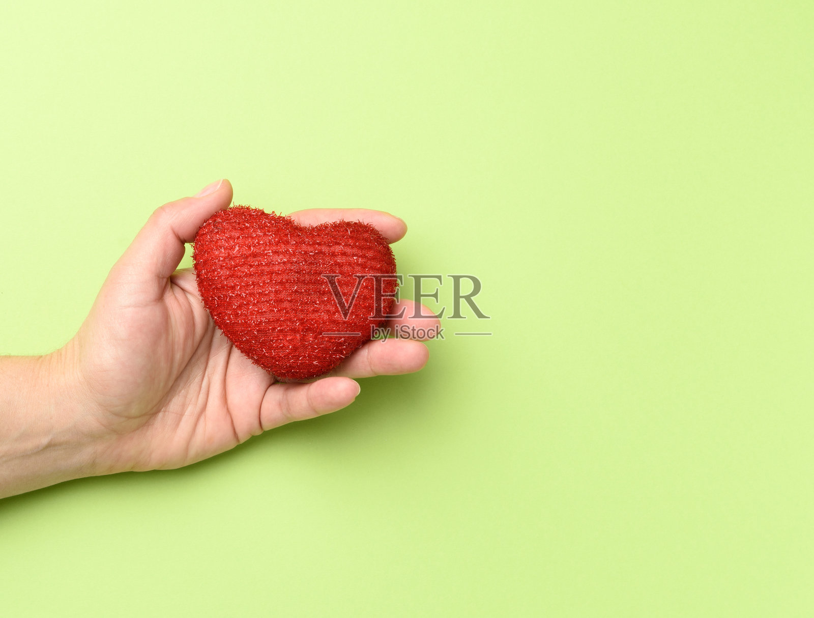 女性手中握着红色的纺织心，绿色的背景照片摄影图片