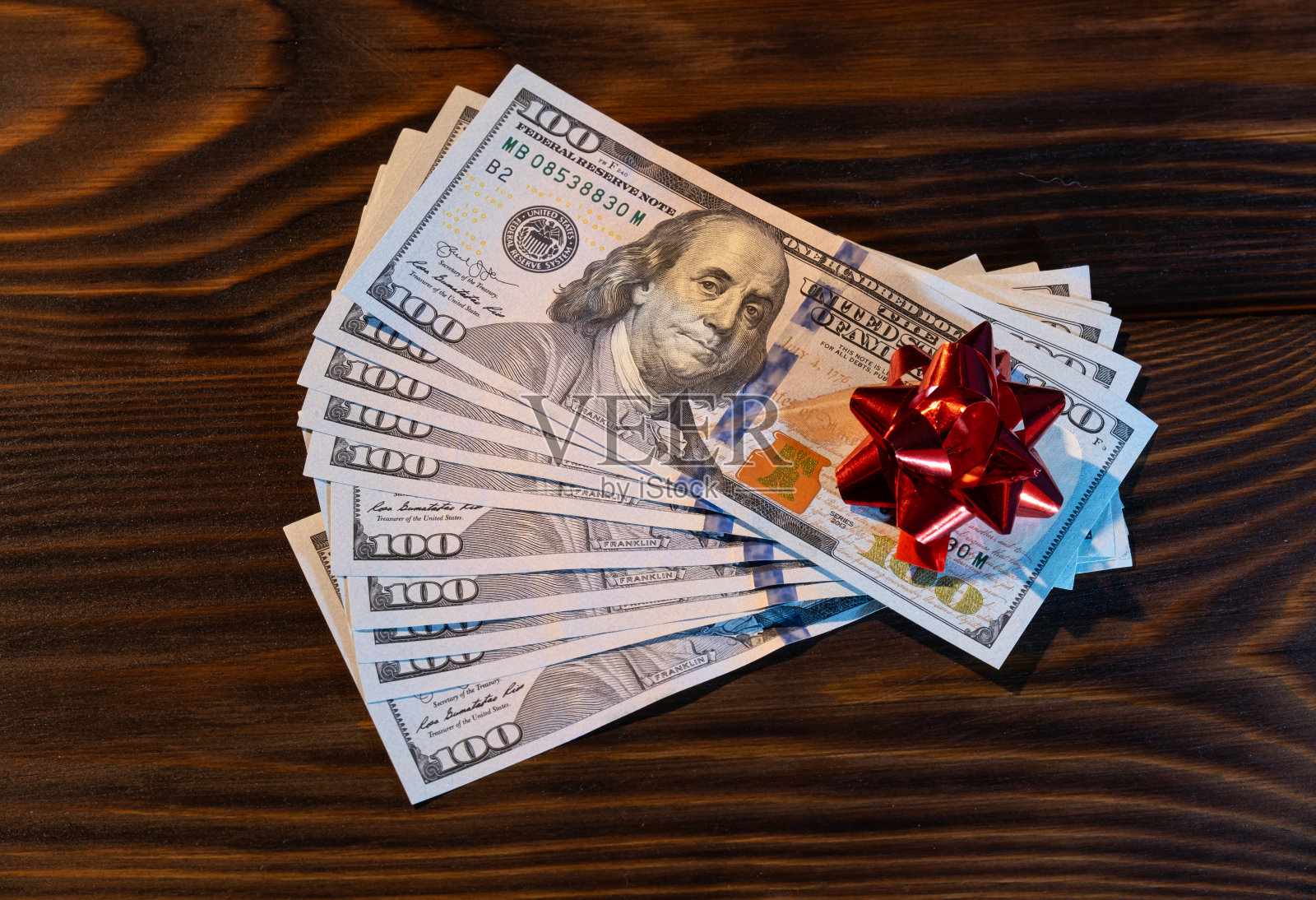 百元钞票堆新年或圣诞节礼物。红蝴蝶结平放在木背景上。俯视图照片摄影图片