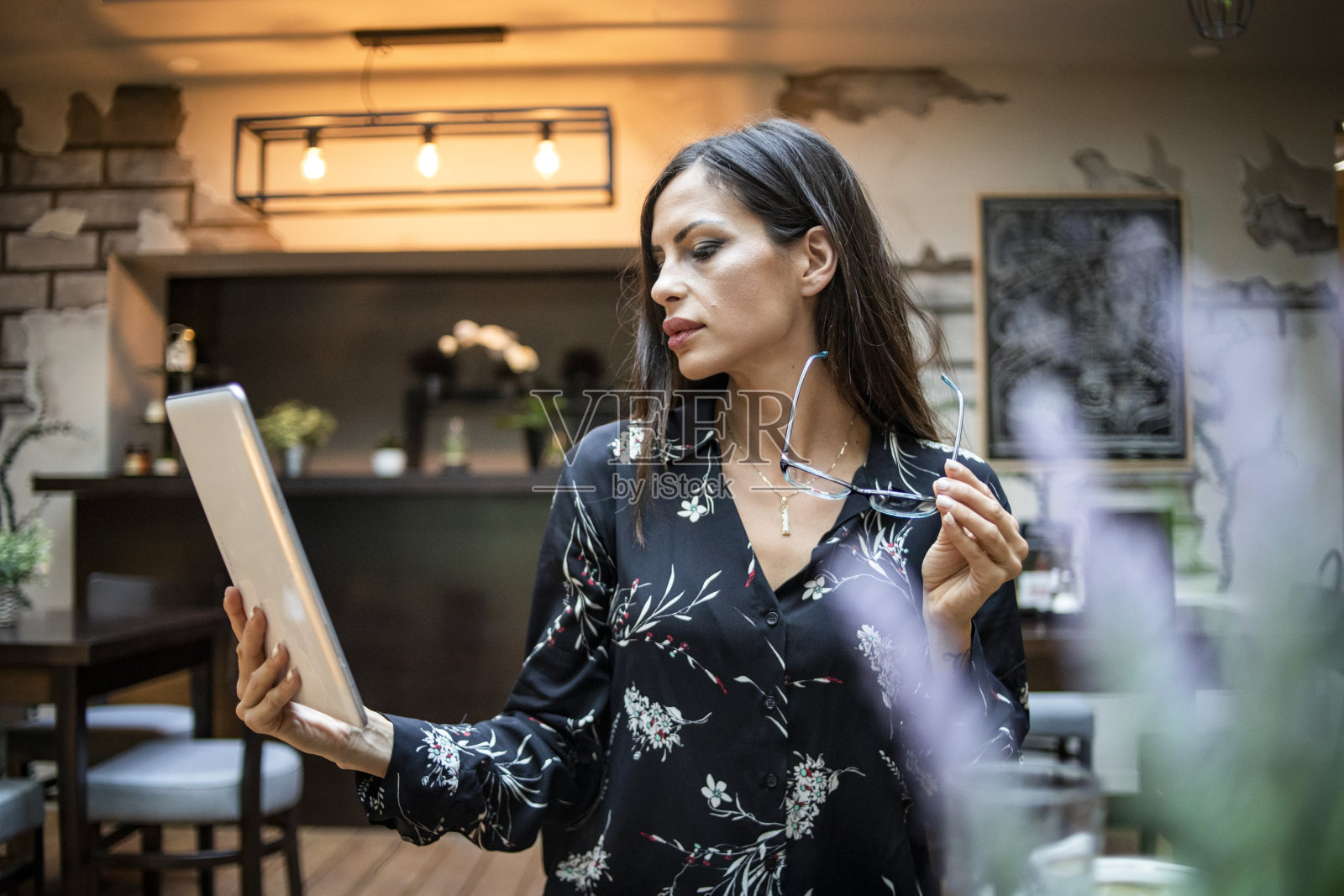 一个女人使用一个数字平板电脑在一个酒吧-美丽的年轻黑人妇女使用平板电脑在一个酒吧，喝咖啡，享受她的自由职业工作照片摄影图片