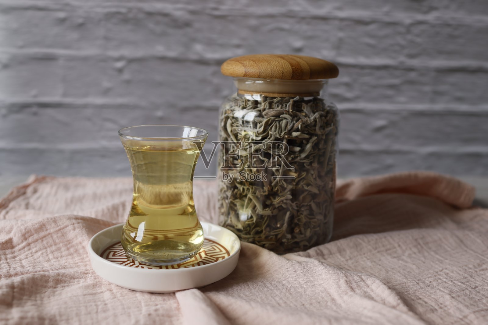 玻璃罐里的鼠尾草和一杯酿造鼠尾草，在粉红色的织物餐巾上，工作室拍摄照片摄影图片