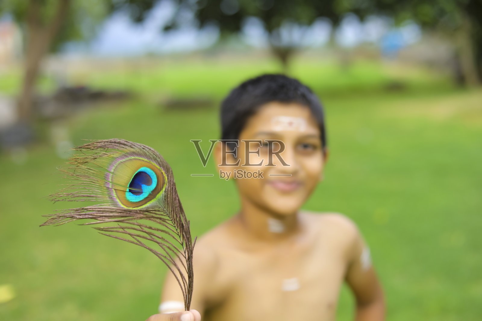 一个印度小孩手里拿着孔雀羽毛，装扮成奎师那神照片摄影图片