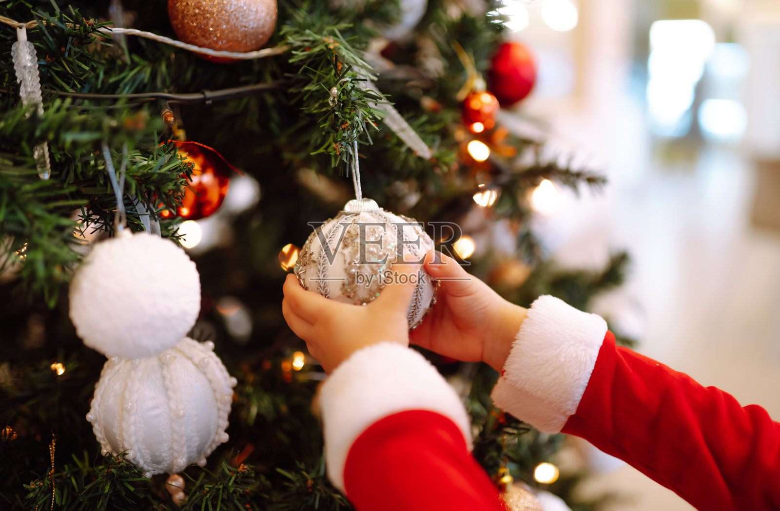 小朋友在圣诞树上挂装饰用的玩具球。照片摄影图片