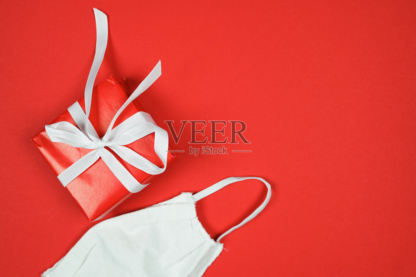 新冠肺炎疫情期间的圣诞节。红底彩带和面具的礼盒照片摄影图片