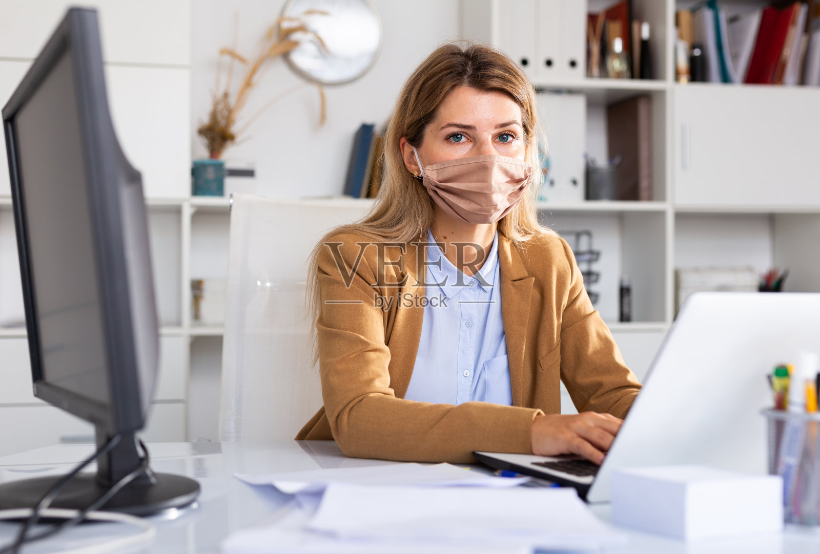 戴面具的女商人在她的白色办公室里工作照片摄影图片