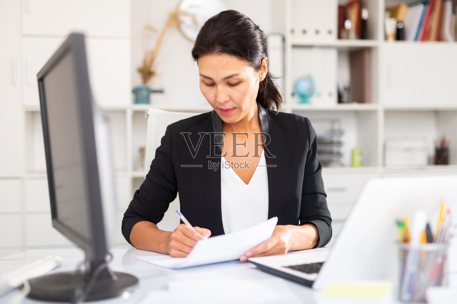 在办公室使用笔记本电脑和文件的女性经理照片摄影图片