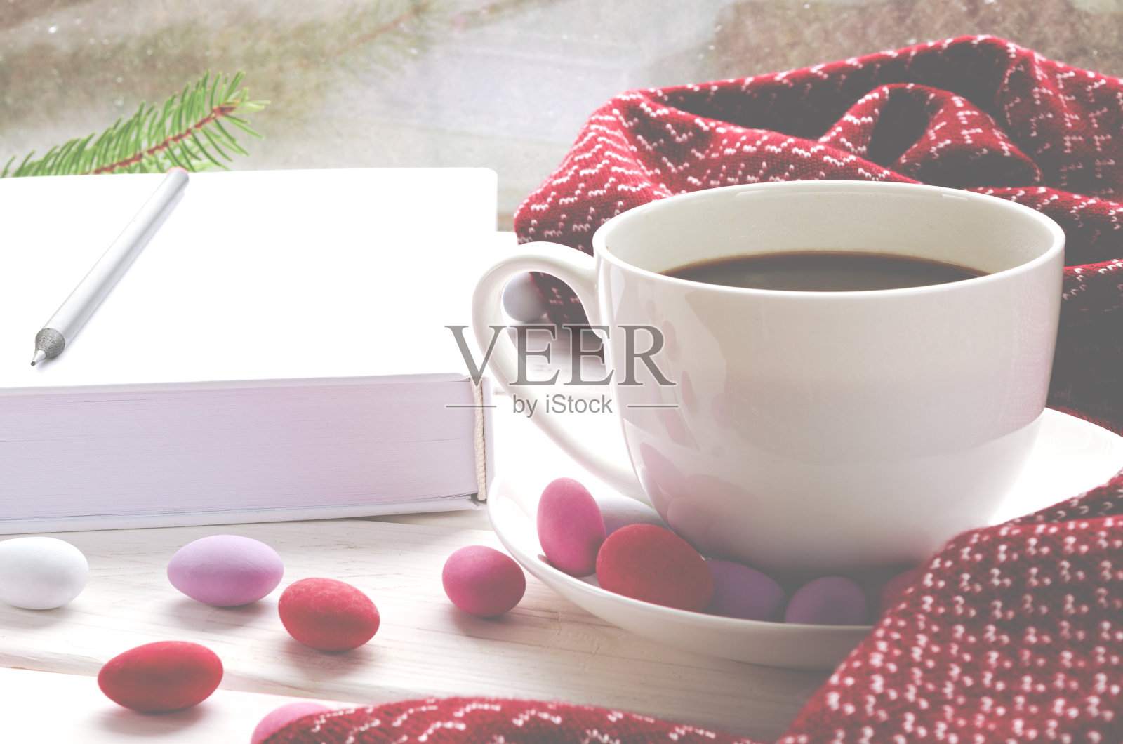 木制窗台上放着一杯白色的咖啡和五颜六色的糖果，旁边是一条温暖的围巾和一本白色的书照片摄影图片