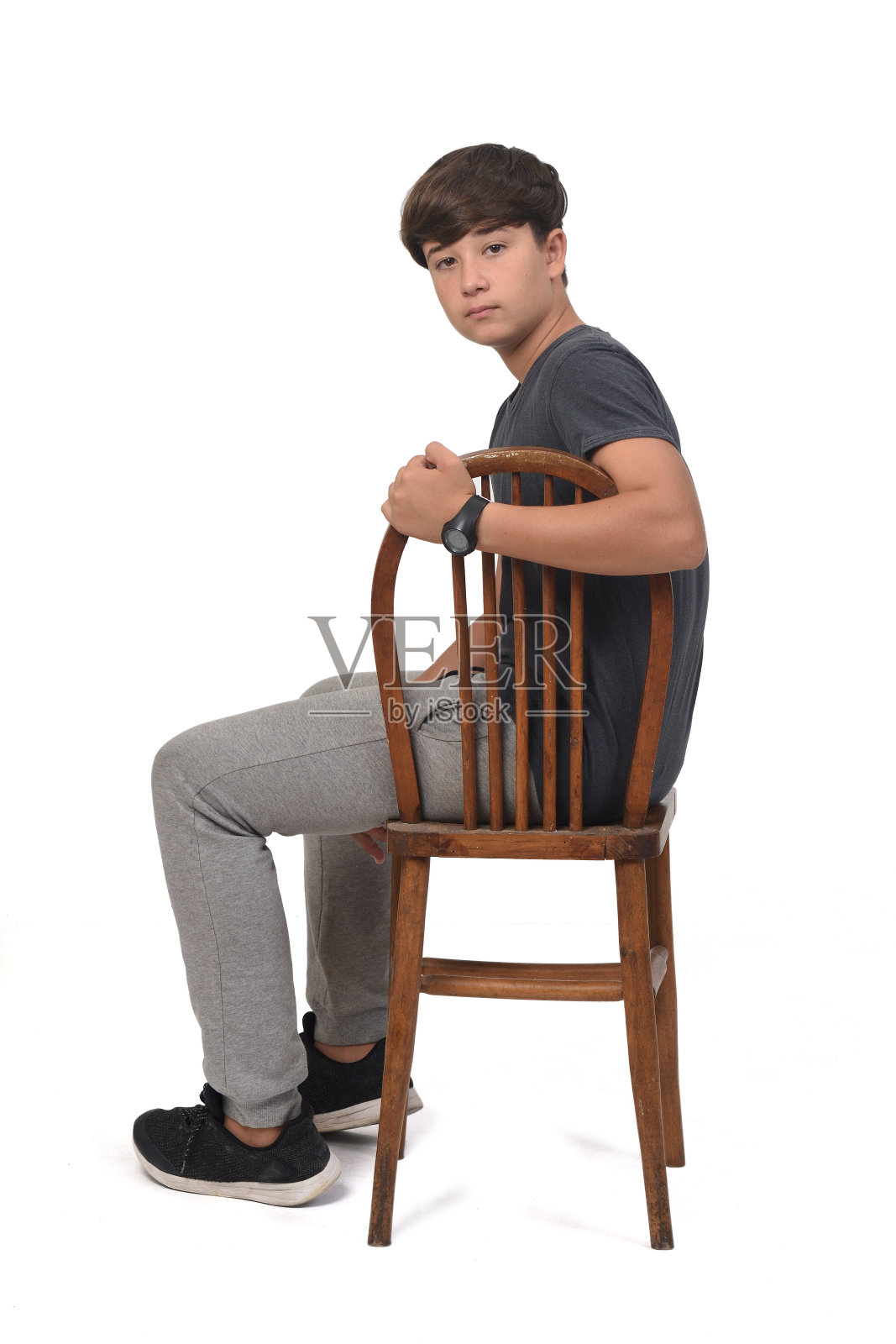 一个十几岁的男孩坐在白色背景的椅子上，照片摄影图片