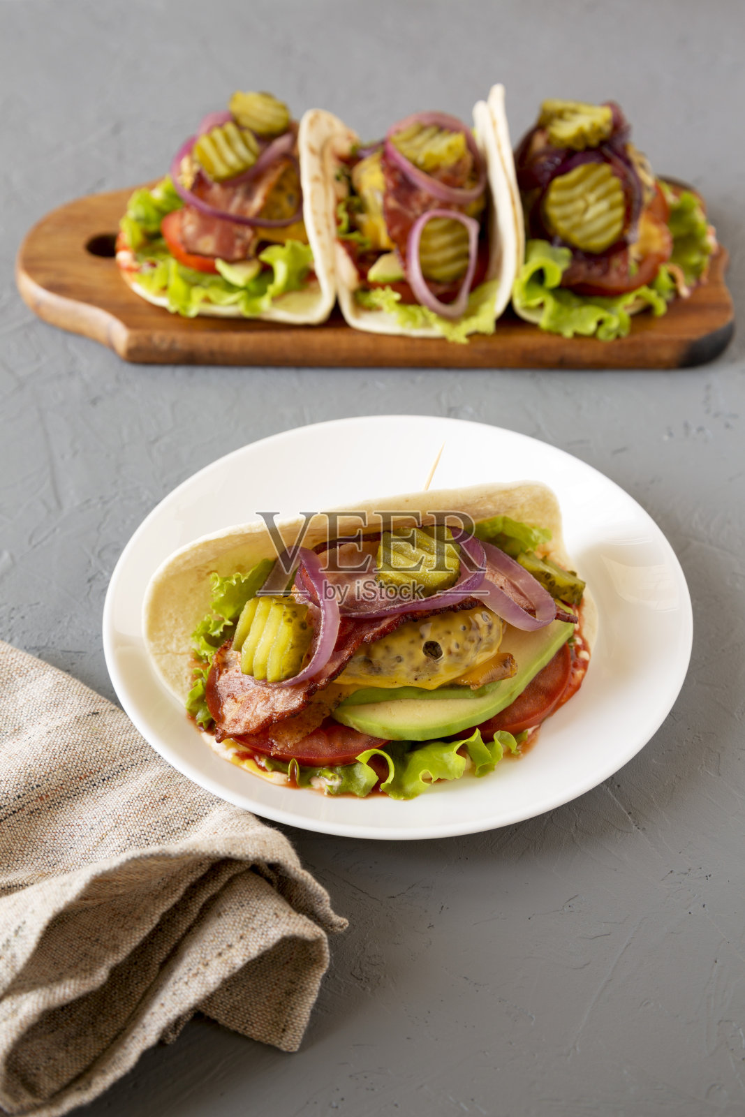 自制培根芝士汉堡墨西哥玉米卷在白色盘子上，灰色的表面，侧视图。副本的空间。照片摄影图片