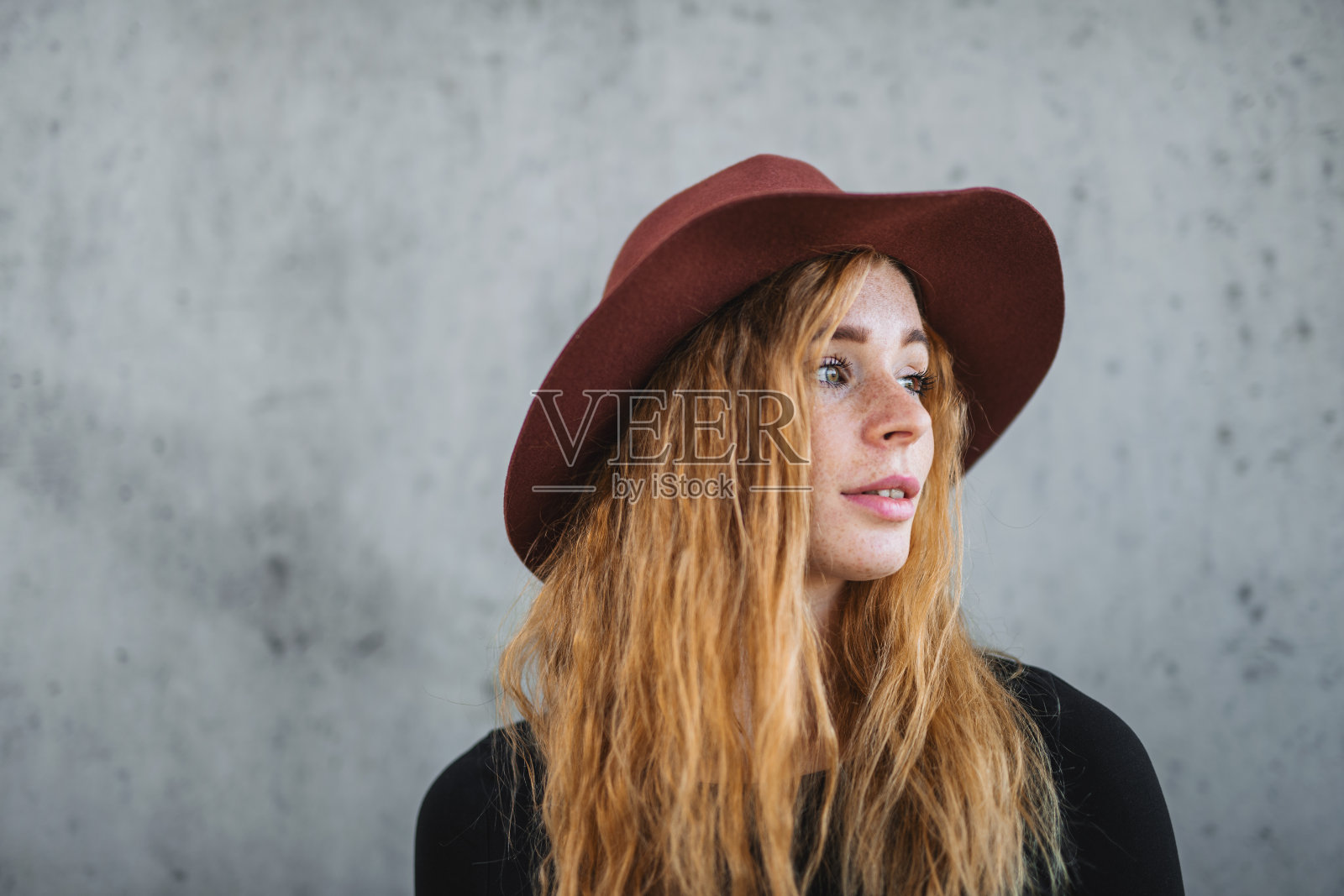 年轻女子的肖像红头发和帽子站在灰色的背景。照片摄影图片