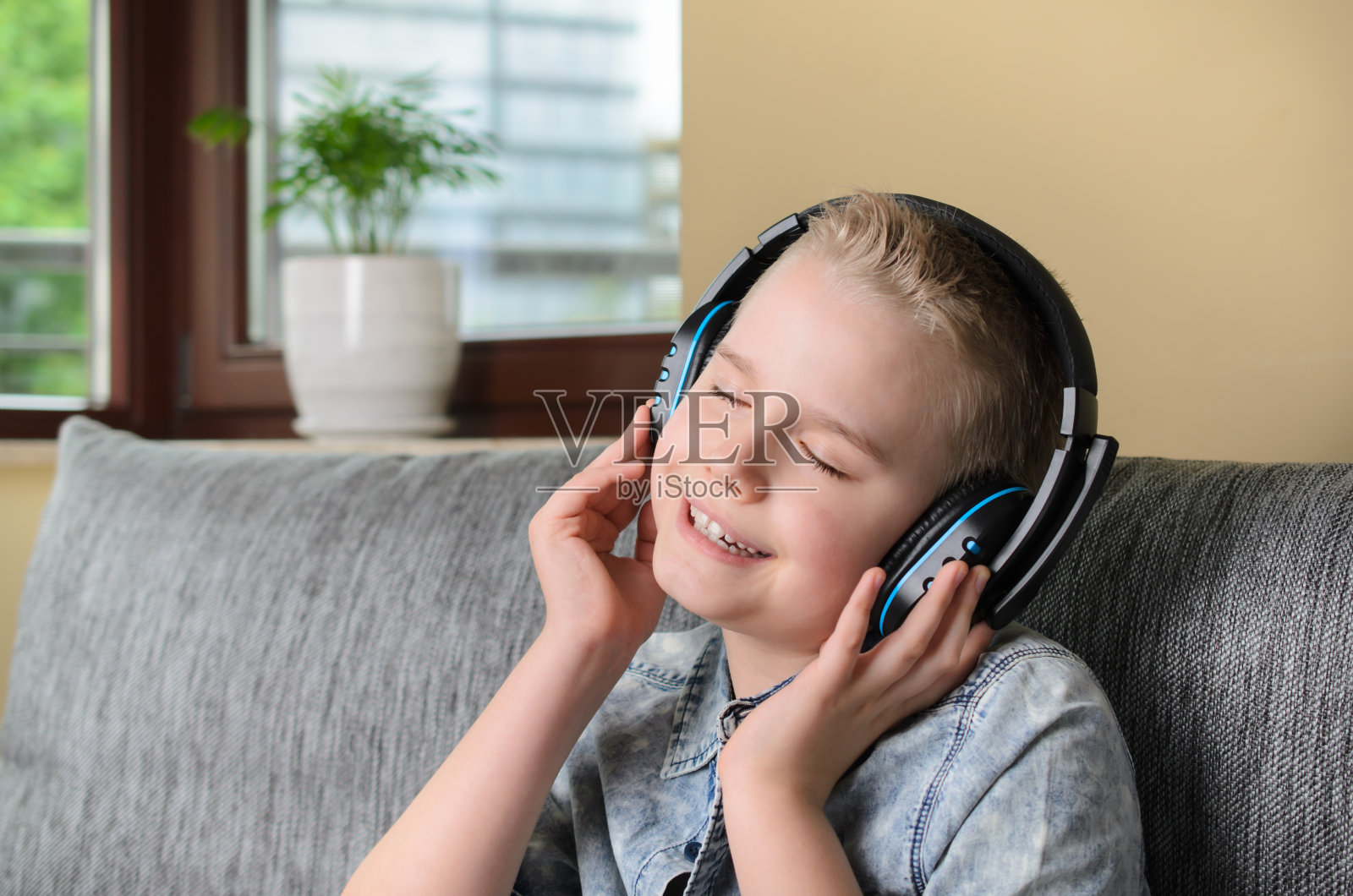 时髦的少年戴着耳机在家里听音乐唱歌。快乐的微笑男孩休息在家里的沙发上照片摄影图片