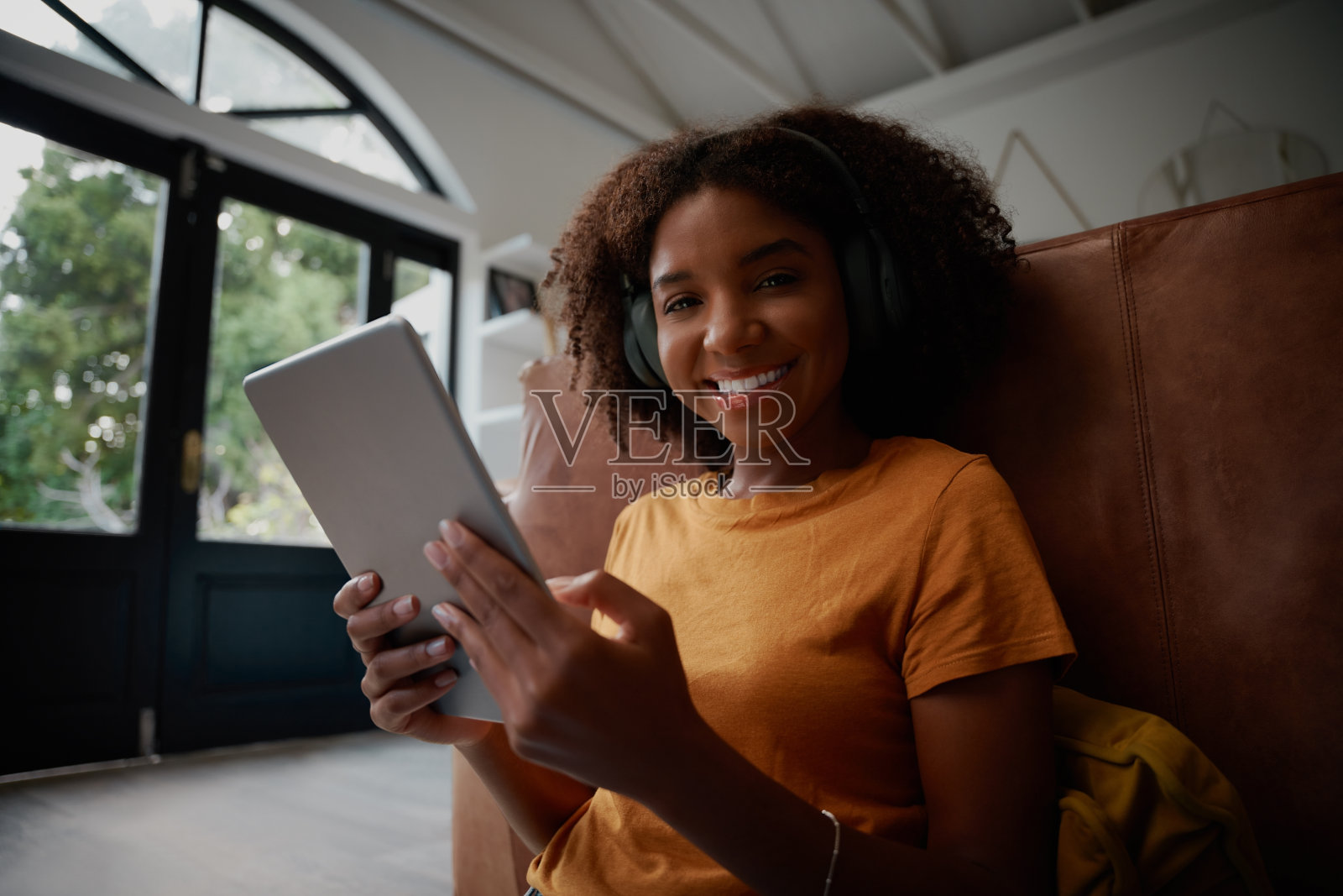 年轻美丽的非洲女人坐在地板上用数码平板电脑和耳机看着相机照片摄影图片