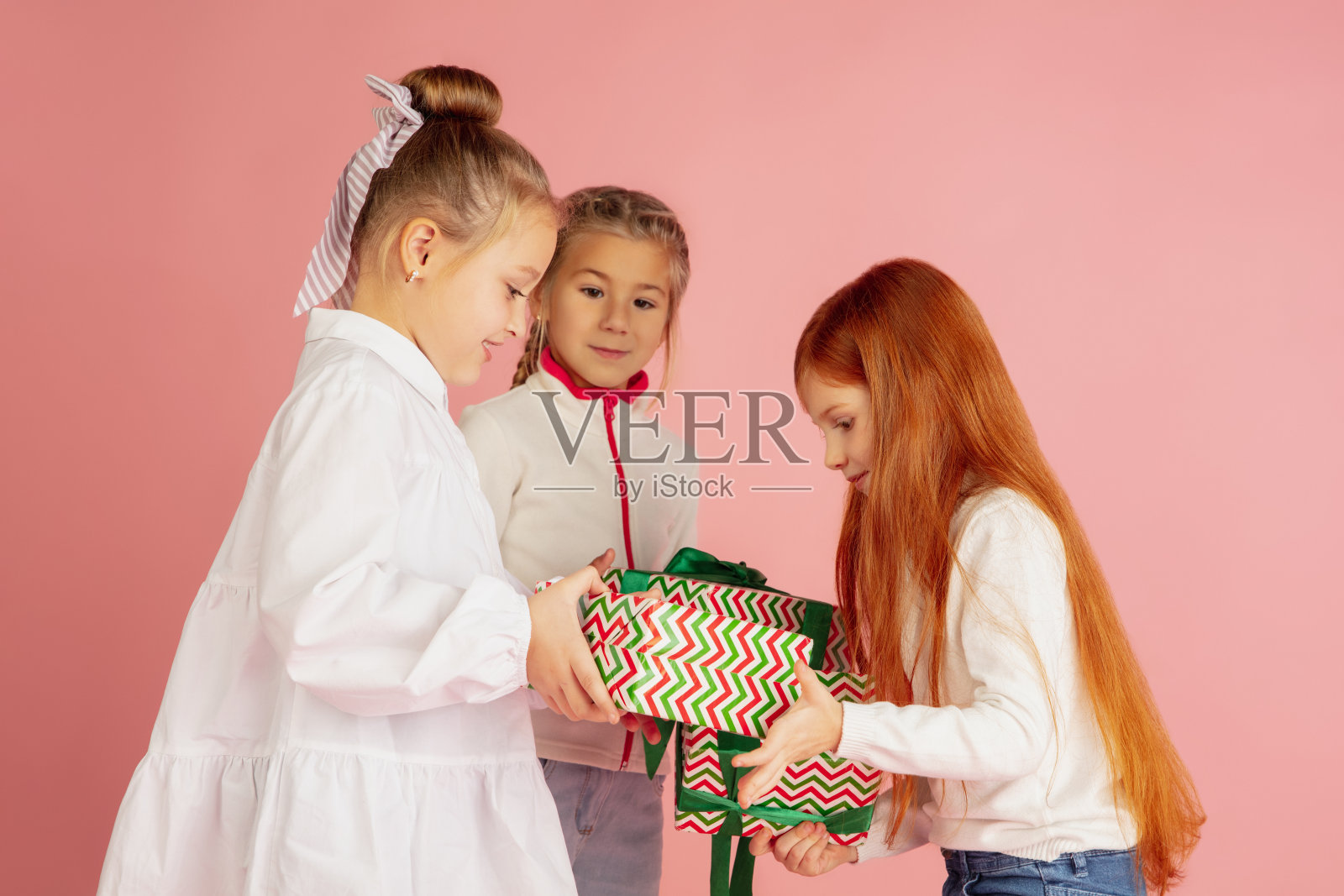 在圣诞节送礼物和收礼物。一群快乐微笑的孩子们在粉红色的工作室背景上玩得很开心照片摄影图片