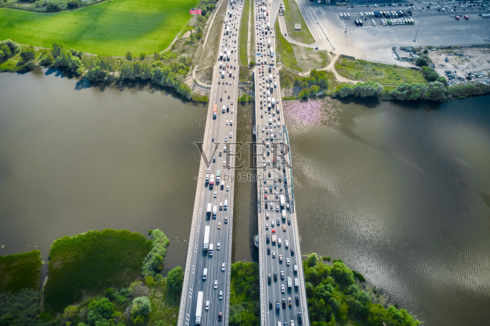 汽车正从河两岸的双桥上飞驰而过。树木在海岸线上。摄像机从这个角度向下看。从无人机上鸟瞰。阳光与阴影。立交桥上两条平行的路。照片摄影图片
