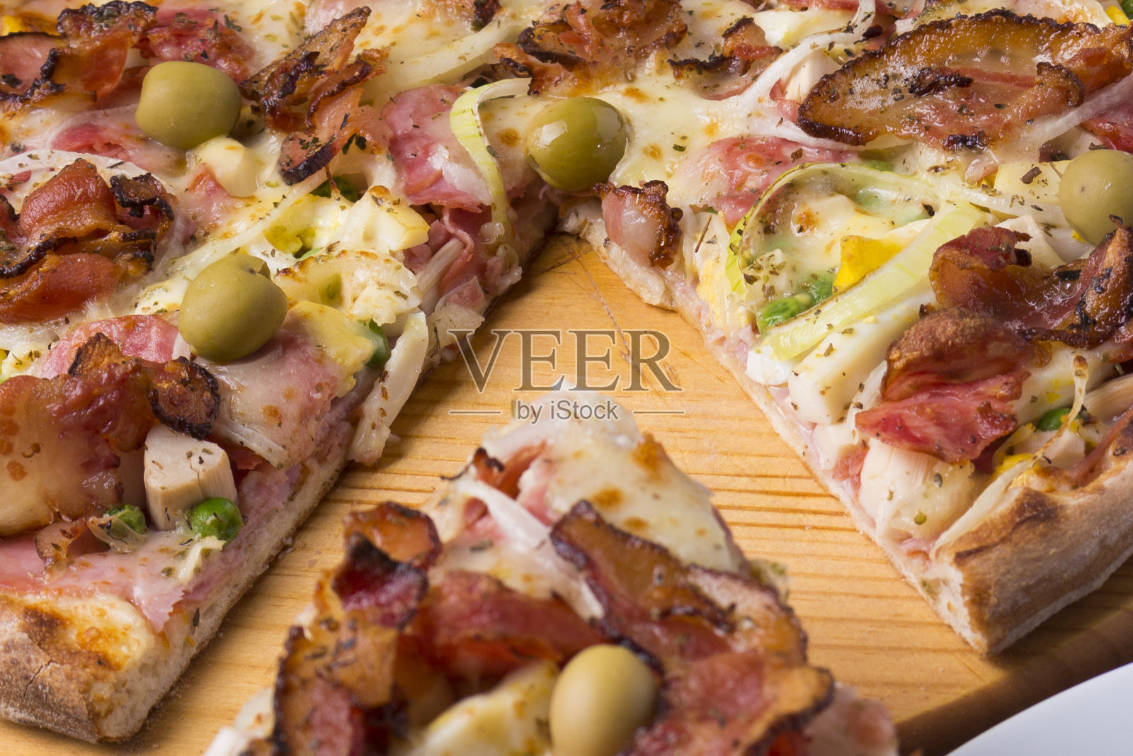 葡萄牙披萨，由火腿、豌豆蛋、棕榈心、意大利辣香肠、洋葱、马苏里拉奶酪和培根制成。一片披萨被提供的特写照片。照片摄影图片