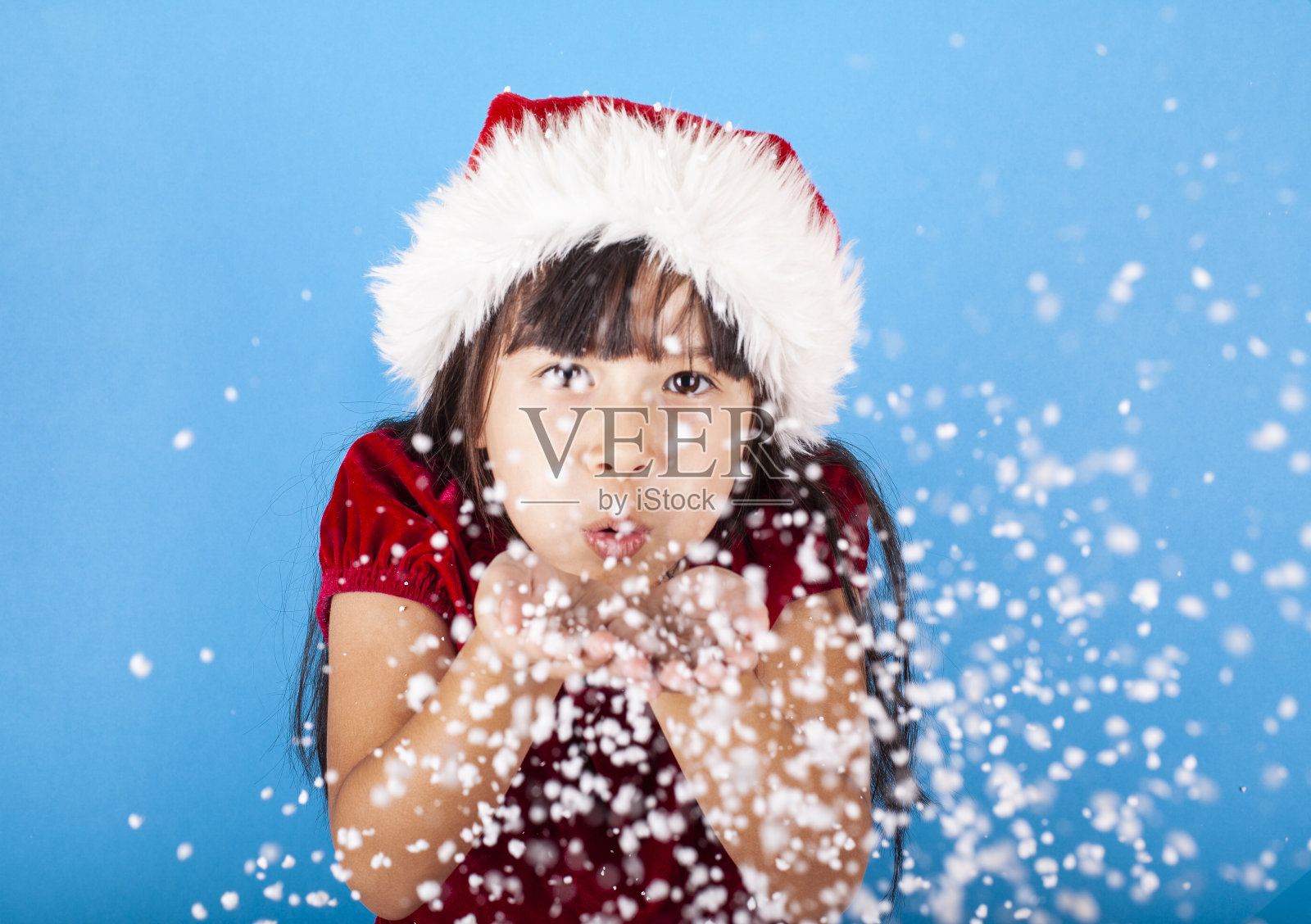 亚洲小女孩戴着圣诞老人的帽子吹雪花照片摄影图片