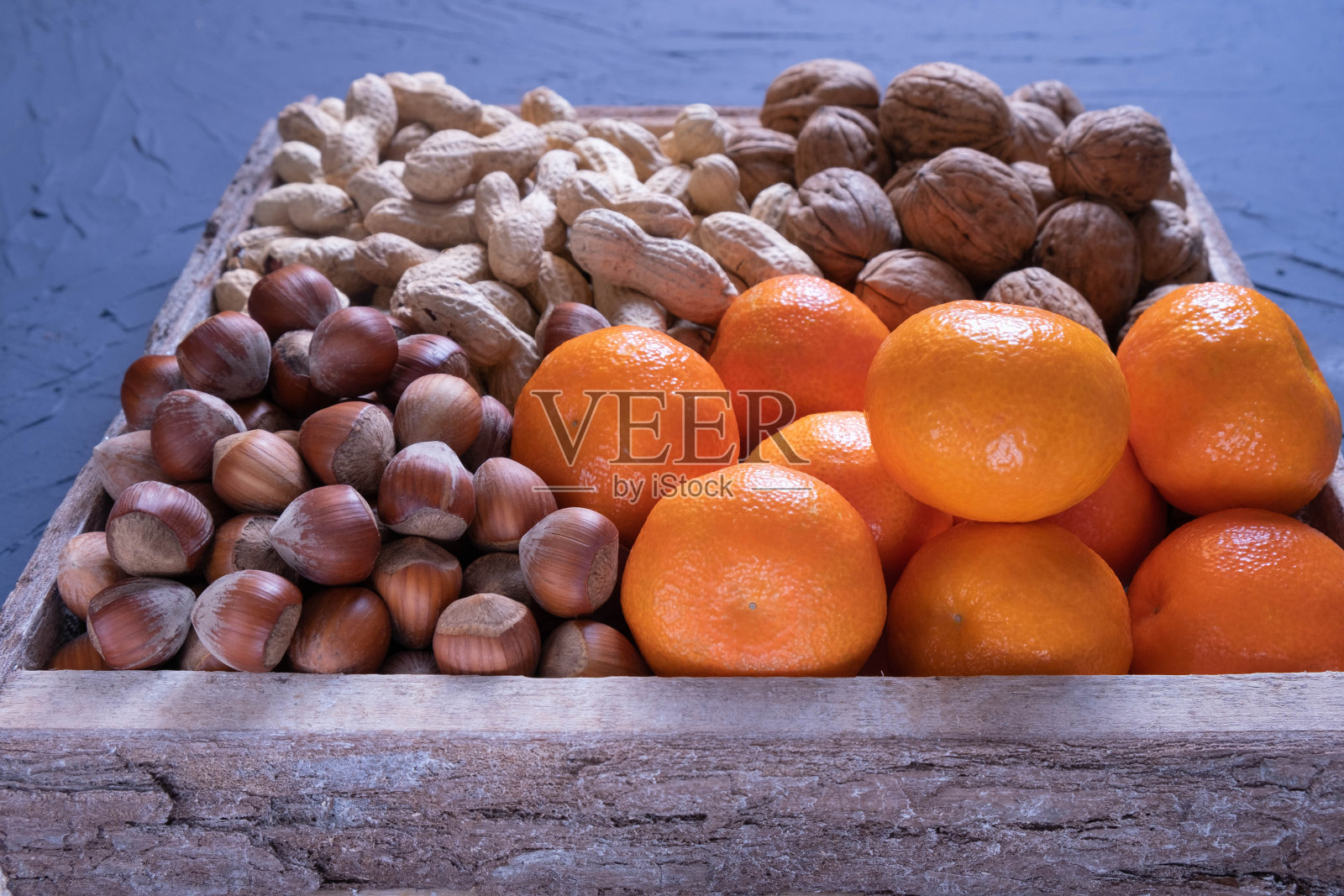 榛果、核桃、花生和橘子放在一个木盒子里，背景是蓝色的纹理照片摄影图片