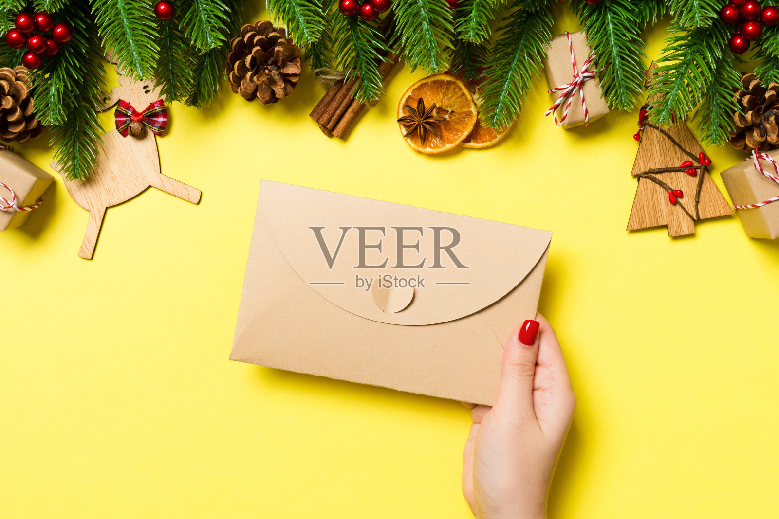 女子在黄色背景上拿着信封的俯视图，背景由节日装饰品制成，圣诞节概念照片摄影图片