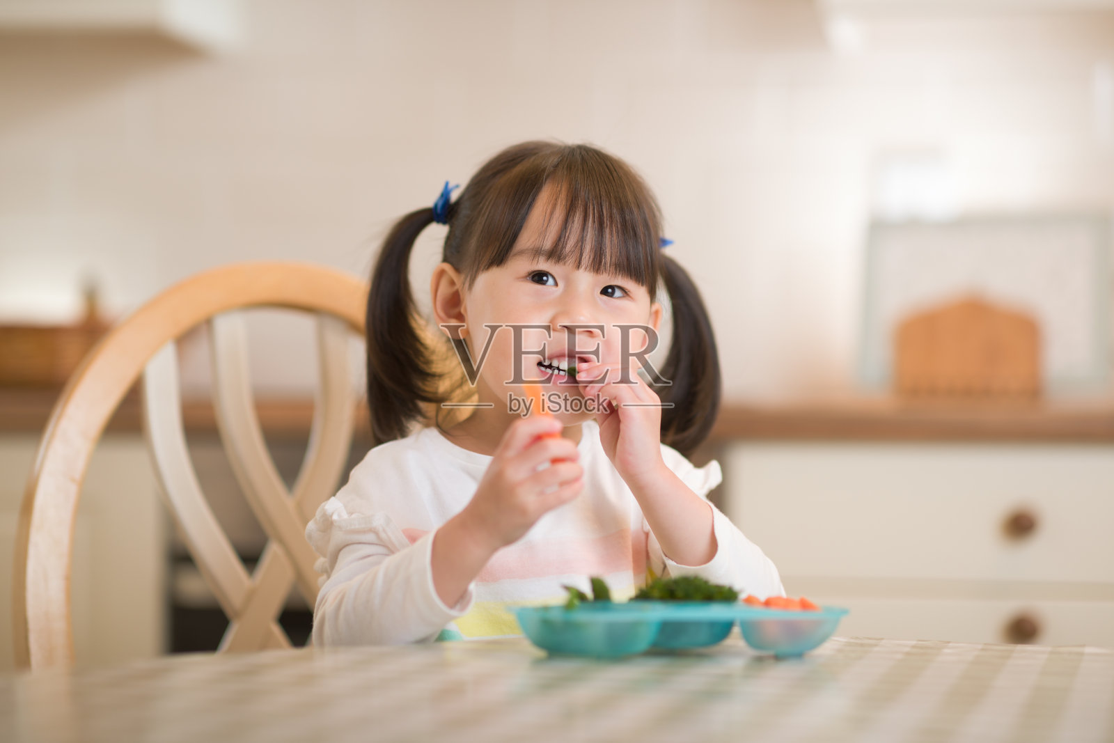 年轻的女孩在真实的厨房背景下吃新鲜的绿色蔬菜照片摄影图片