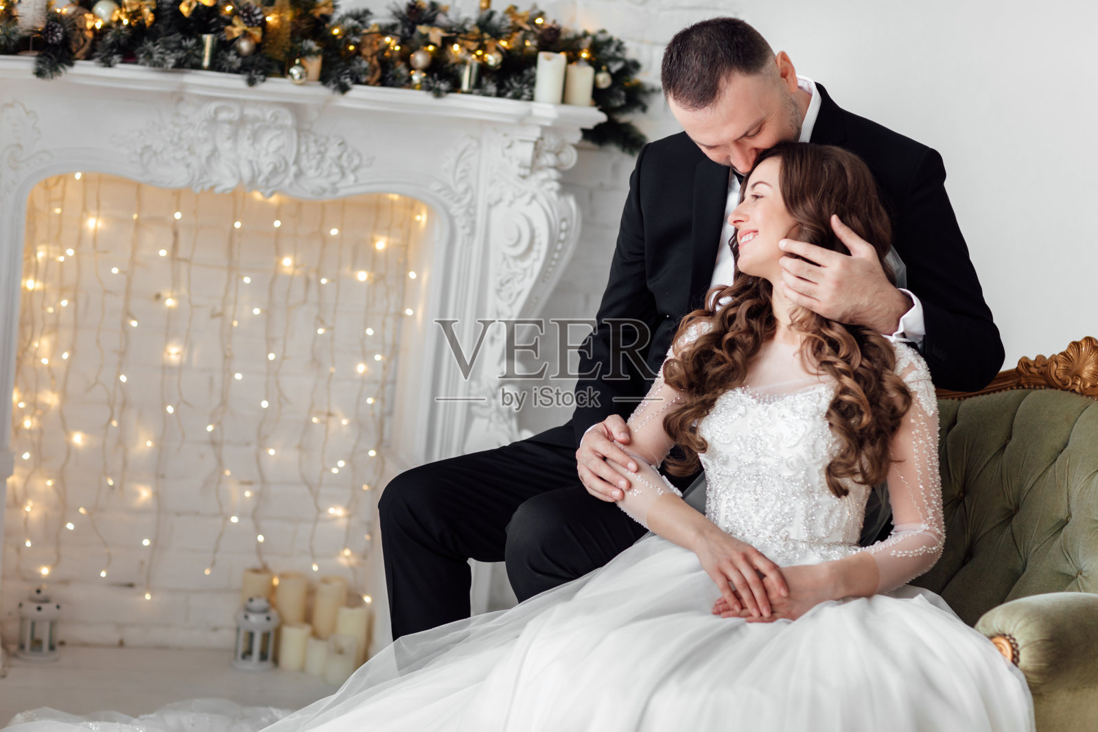 年轻夫妇在爱新娘和新郎摆姿势在工作室的背景装饰圣诞树在他们的婚礼当天在圣诞节。享受幸福和爱的时刻。照片摄影图片