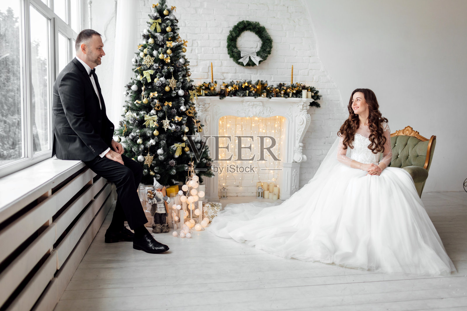 年轻夫妇在爱新娘和新郎摆姿势在工作室的背景装饰圣诞树在他们的婚礼当天在圣诞节。享受幸福和爱的时刻。照片摄影图片