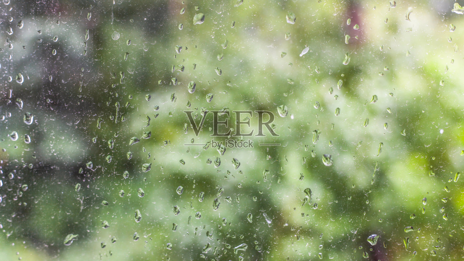 雨滴落在玻璃上，绿色植物在背景上模糊了照片摄影图片