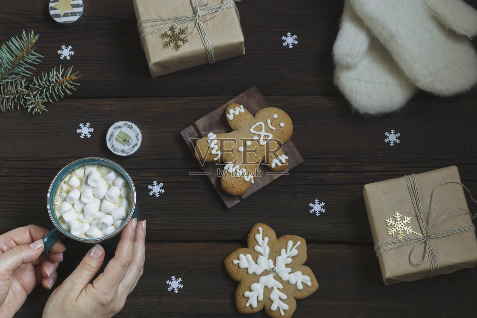 女人手里捧着一杯用棉花糖烫的饮料。温暖的白色手套，新年礼物，姜饼，深色木质背景上的蜡烛。圣诞贺卡。从上面的观点照片摄影图片
