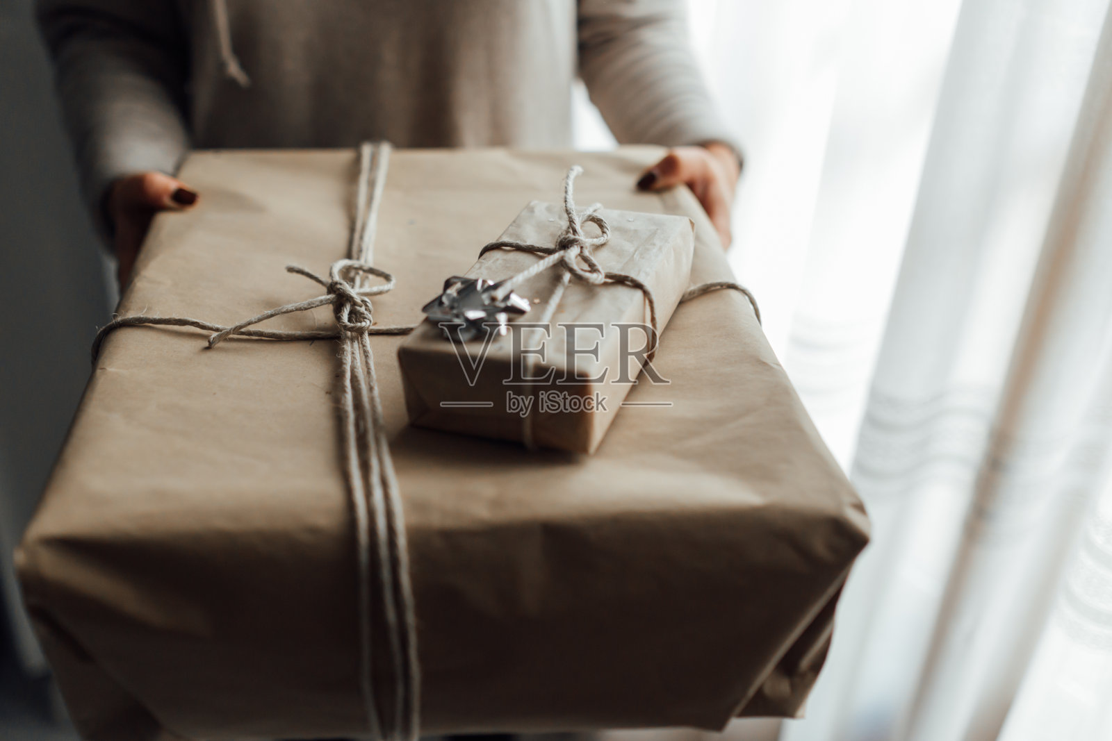 年轻女子手里拿着用牛皮纸和杜松树叠起来的圣诞礼品盒。圣诞礼物的概念。照片摄影图片