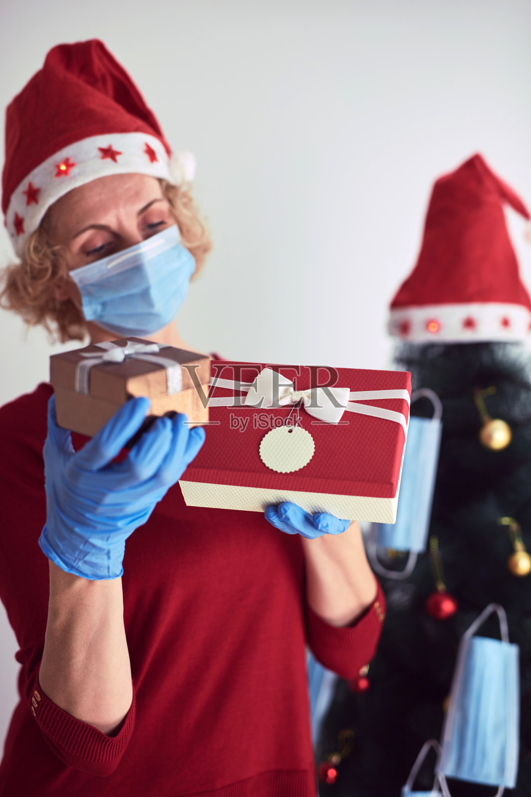 在2020 / 2021年病毒大流行期间，手持礼盒的妇女用医用口罩装饰圣诞树。照片摄影图片