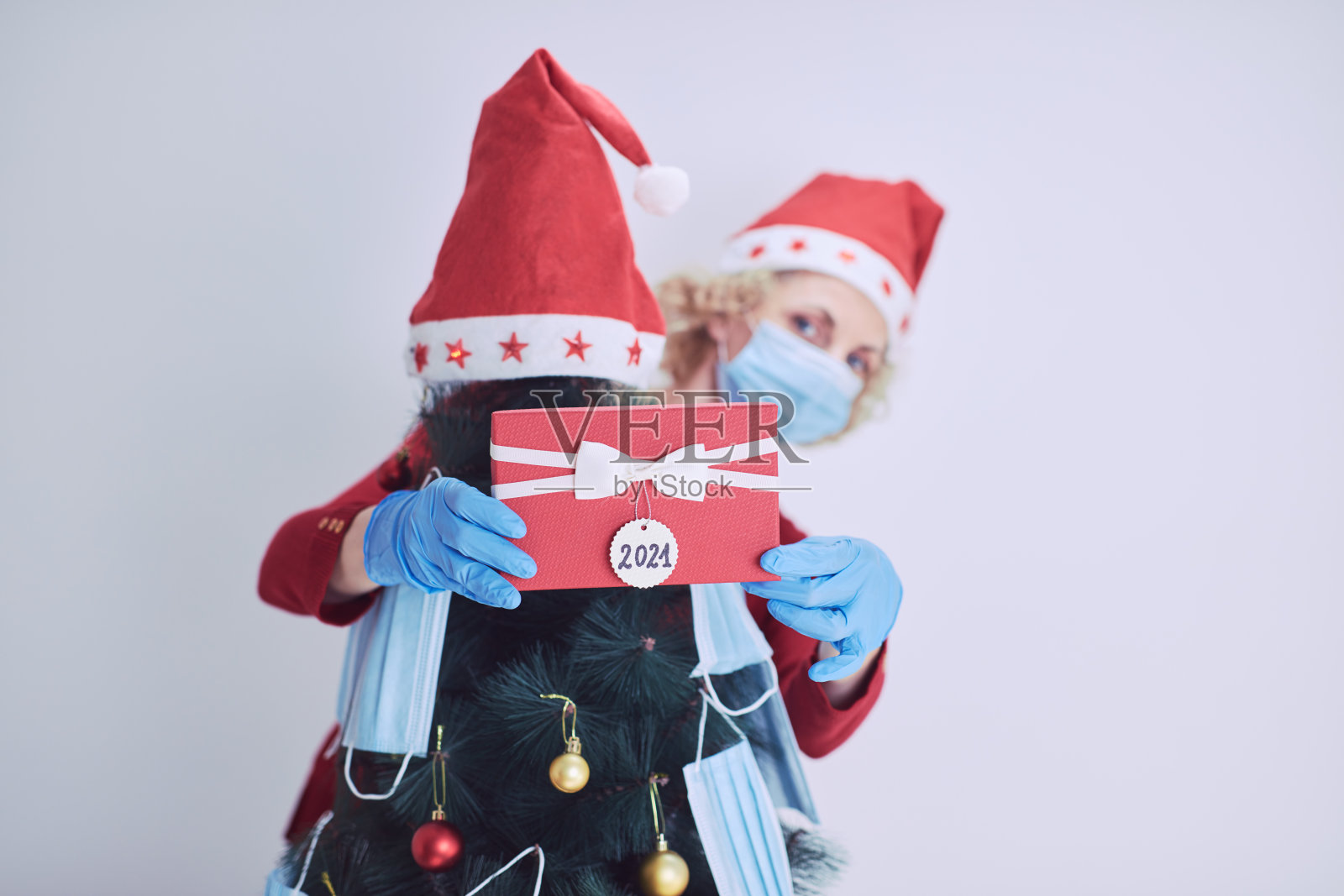 在2020 / 2021年病毒大流行期间，妇女拿着礼盒礼物，用医用口罩装饰圣诞树。照片摄影图片
