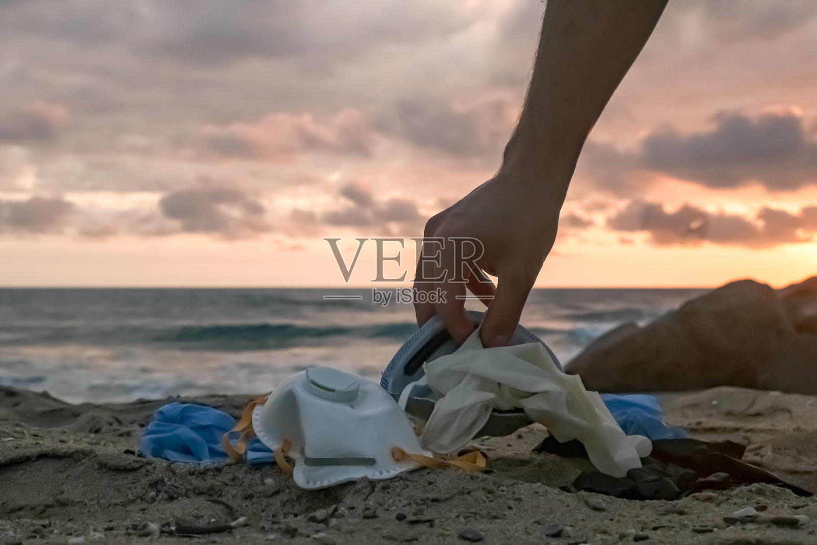 男子用手收集医疗垃圾、口罩和塑料手套等垃圾，在日落海边捡拾新冠病毒污染疾病垃圾照片摄影图片