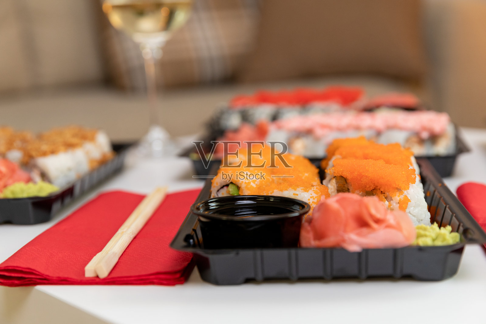 在一个舒适的房间里，白色的桌子上放着一套彩色的寿司和葡萄酒。照片摄影图片