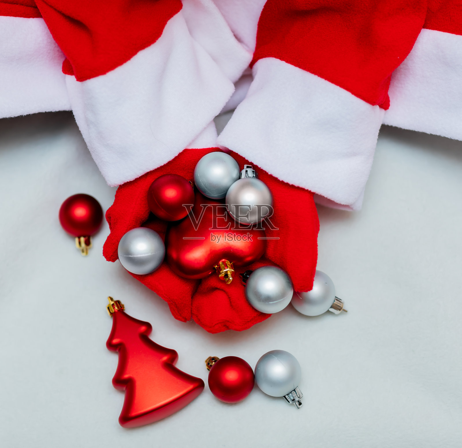 戴着红色手套的手拿着红色和银色的圣诞球在灯光背景上。圣诞节，新年，圣诞老人，2021年。前视图。照片摄影图片