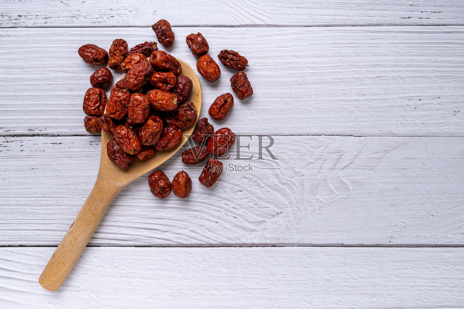 木勺干枣，白木背景。这种水果是一种传统的中国草药。红枣是维生素的来源，是一种健康饮料。照片摄影图片