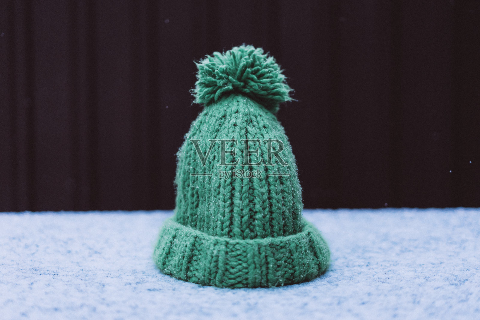 绿色编织的帽子上有一个绒球覆盖着雪，从雪滴下来，先湿雪，选择性对焦，胶卷和谷粒照片照片摄影图片