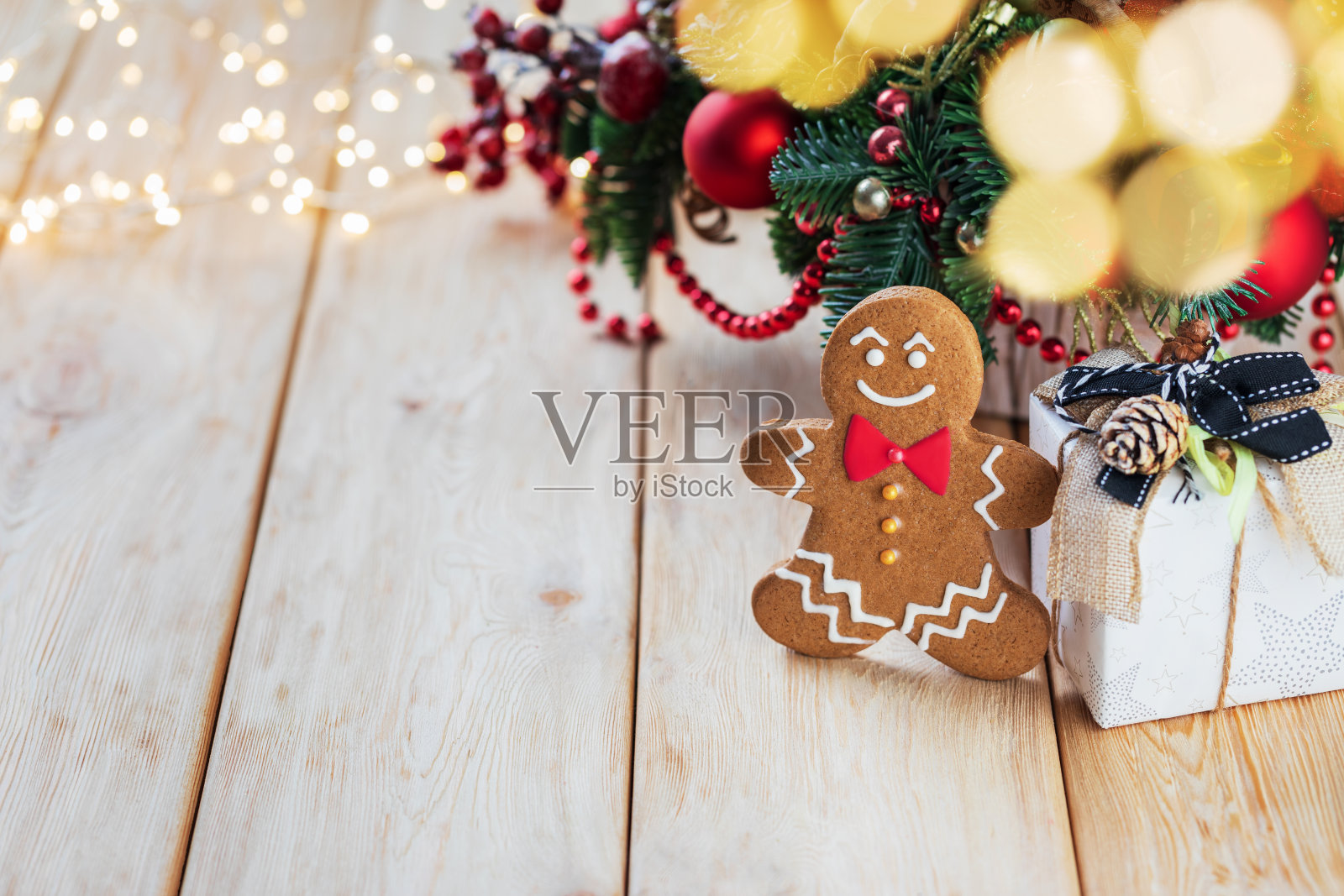 姜饼人饼干和礼盒放在质朴的木桌上，背景是模糊的圣诞彩灯和圣诞装饰品。理想的产品展示和您的文字。照片摄影图片