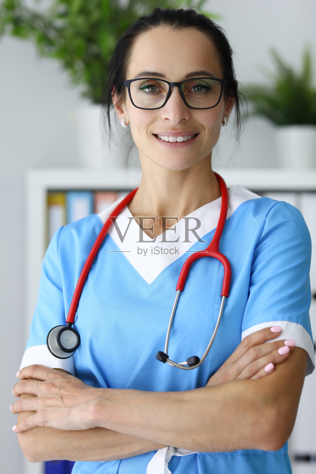 戴眼镜和听诊器的女医务工作者站立着，双臂交叉放在胸前照片摄影图片