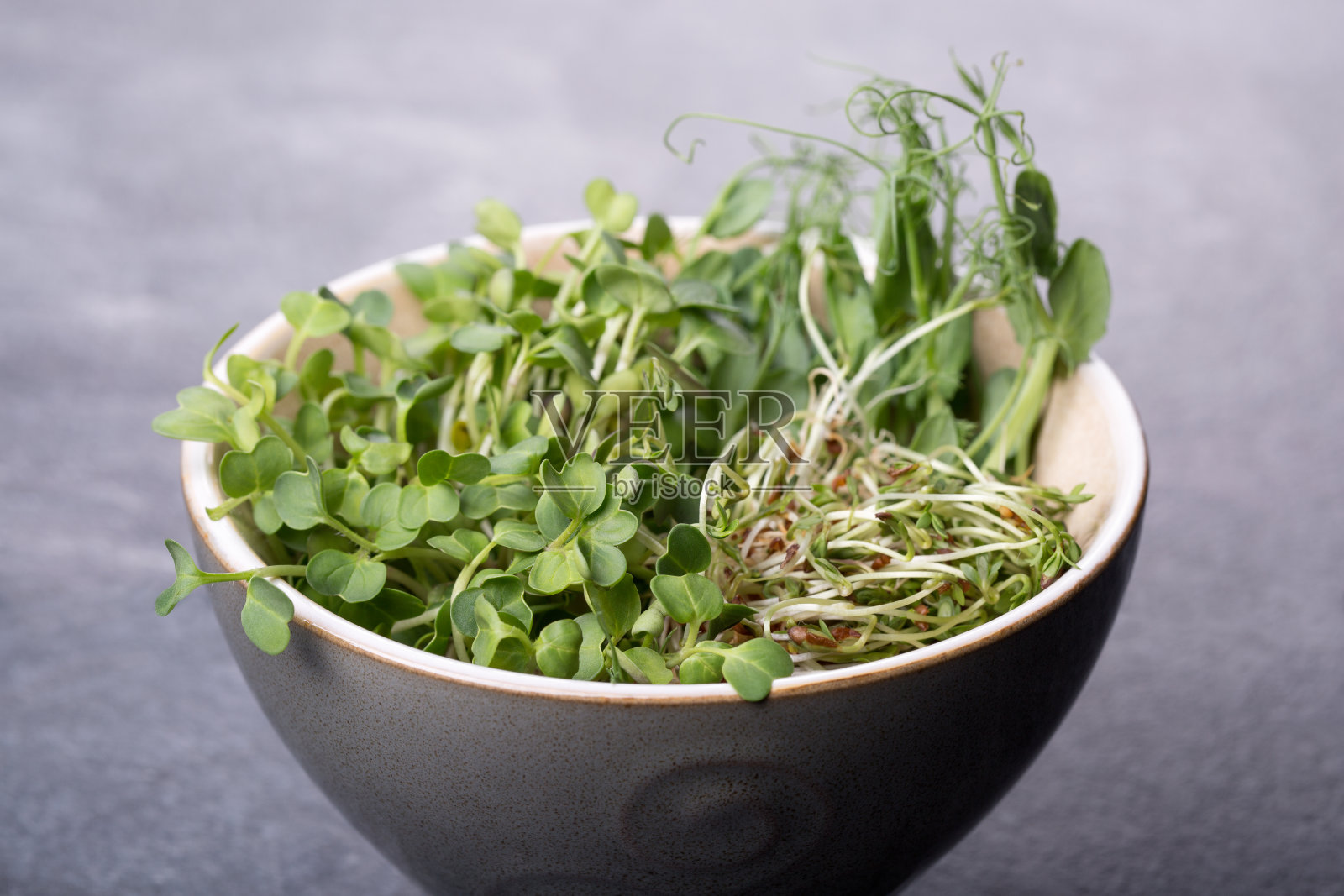 深色表面上的一碗微绿。照片摄影图片