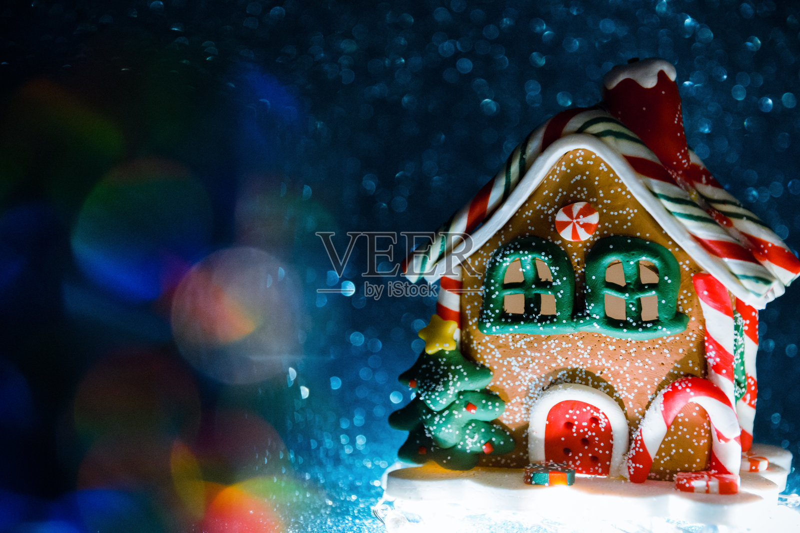 圣诞玩具，在一个姜饼房子的形式从下面发光的蓝色闪光背景与全息辉光。有选择性的重点照片摄影图片