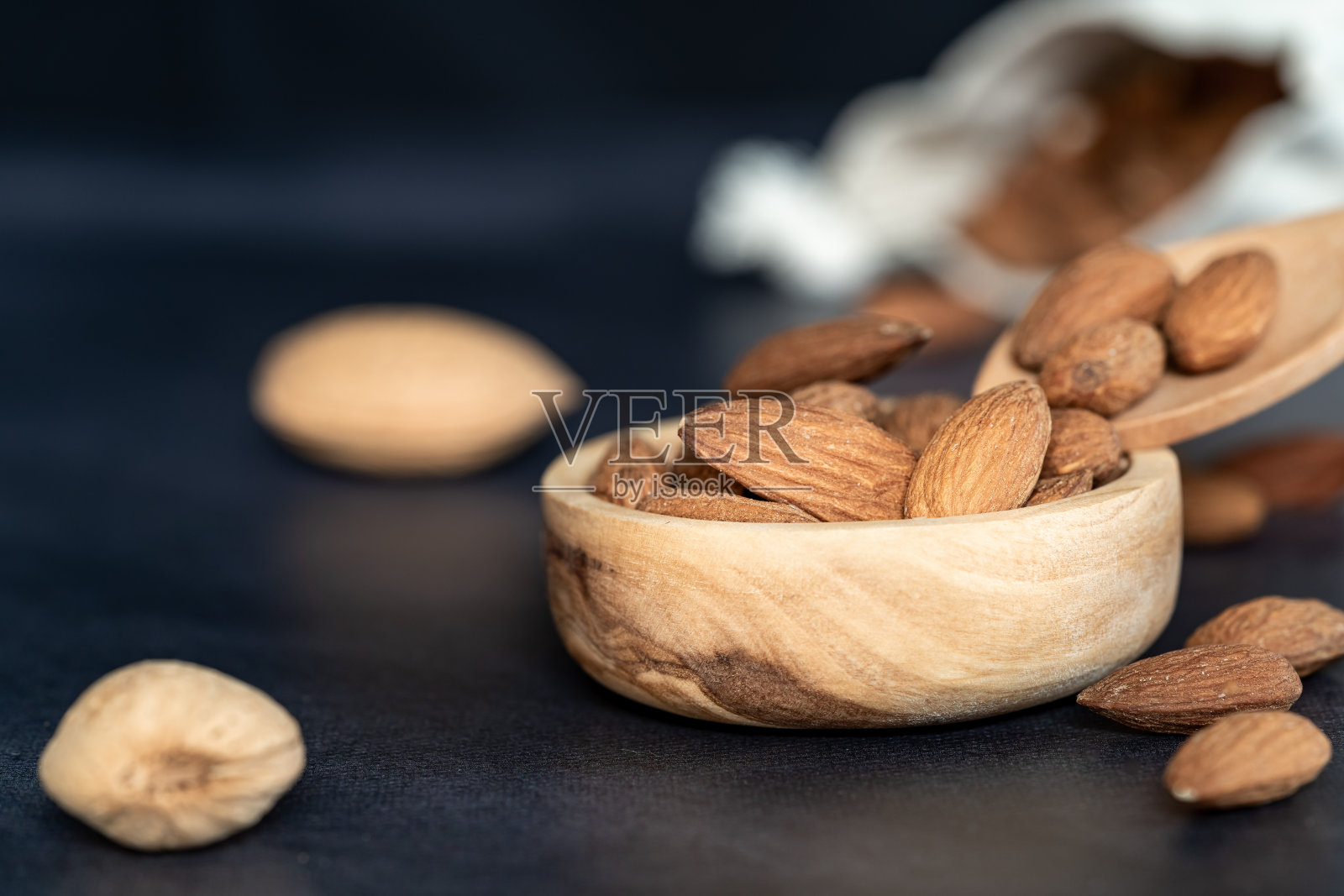木碗里放杏仁，木勺放在黑色木桌上。有些水果装在棉网环保袋里照片摄影图片