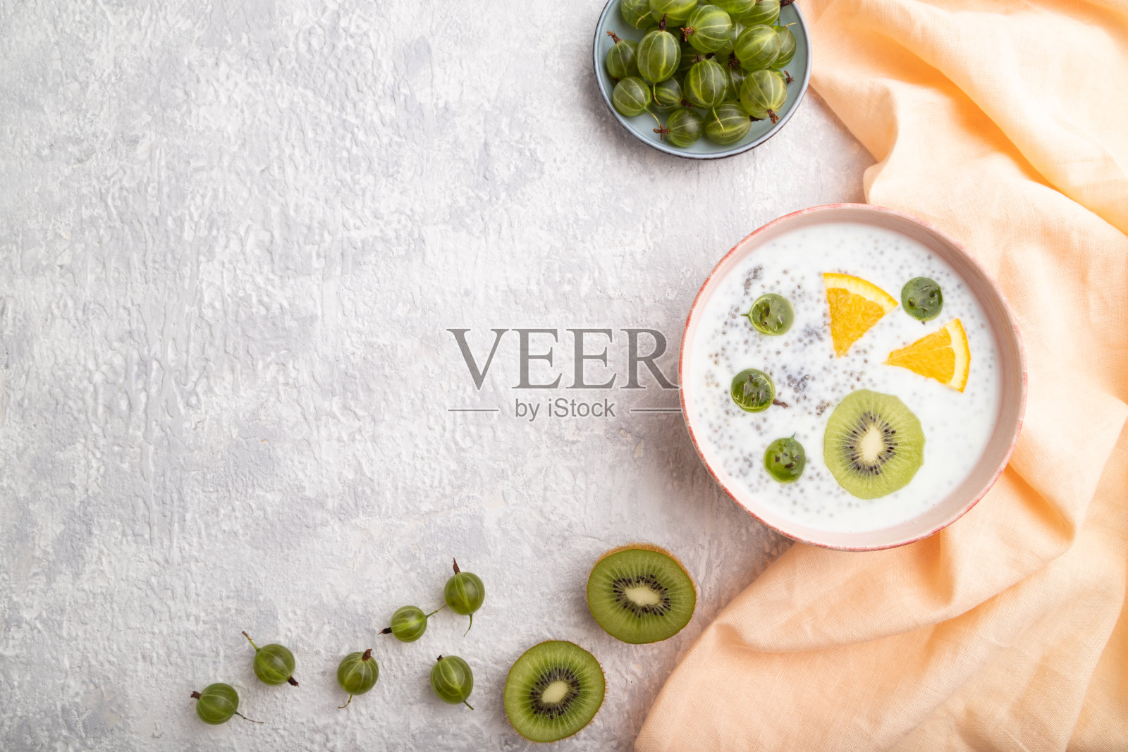 酸奶与猕猴桃，醋栗，嘉在陶瓷碗在灰色混凝土背景和橙色亚麻织物。俯视图，平放，复制空间。照片摄影图片