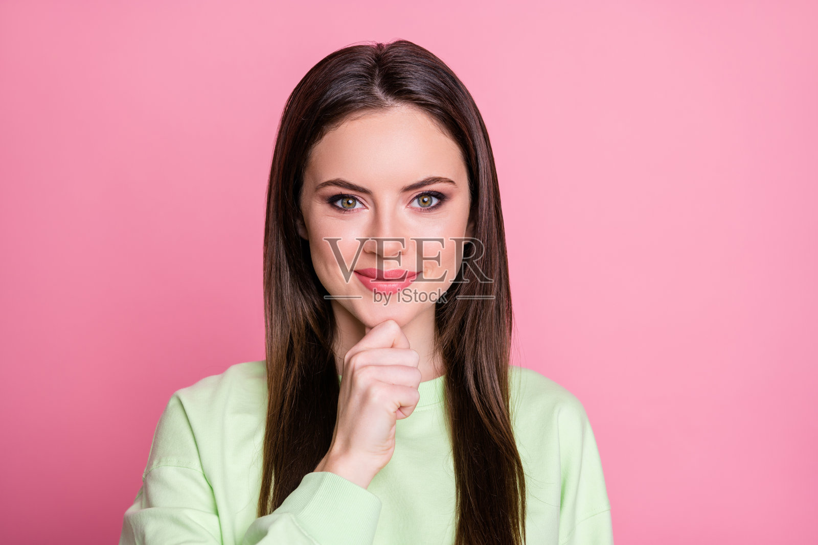 滑稽迷人的女士直长发手手指在下巴聪明有创意的人友好的微笑穿着休闲的绿色运动衫套头衫孤立的粉红色背景的特写照片照片摄影图片
