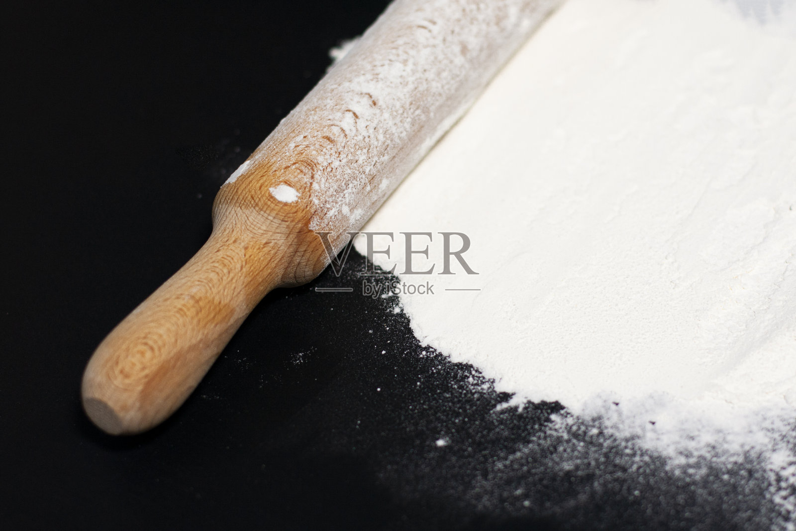 屏幕右上角深色的表面上有一堆白面粉。滚销位于对角线上。照片摄影图片