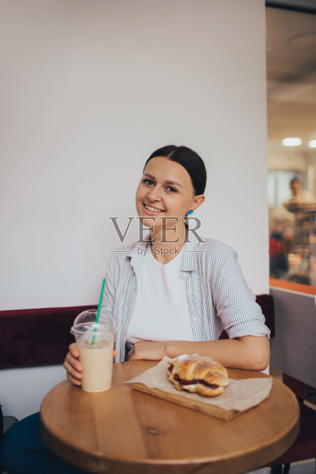美丽的白人女孩坐在现代咖啡店里喝着咖啡吃着羊角面包。照片摄影图片