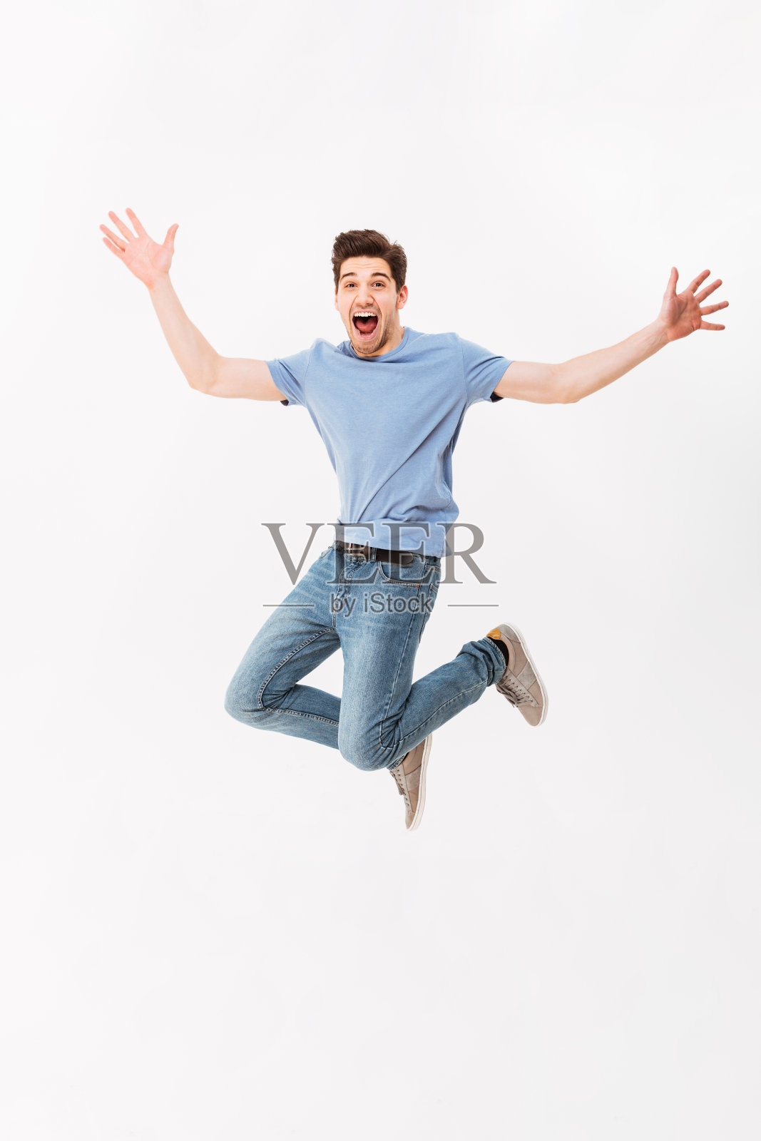 全长照片有趣的男人30岁在休闲t恤和牛仔裤跳手臂向上，孤立在白色的背景照片摄影图片