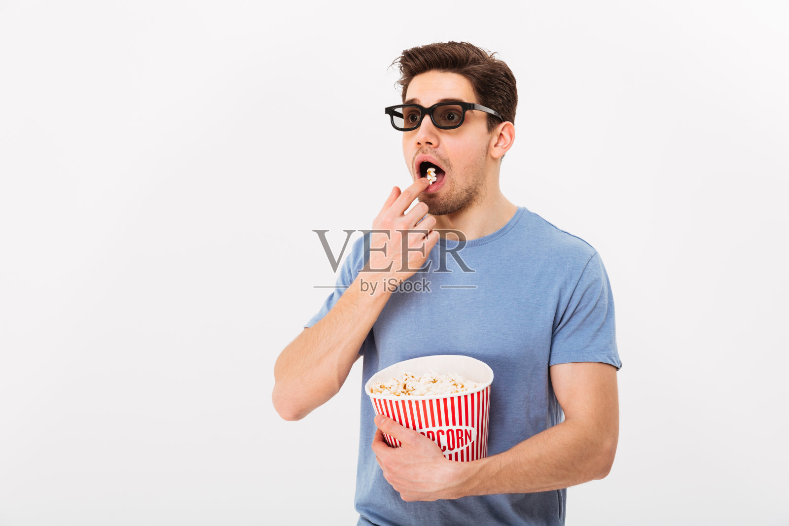 穿着t恤戴着3d眼镜吃爆米花的惊讶男人照片摄影图片