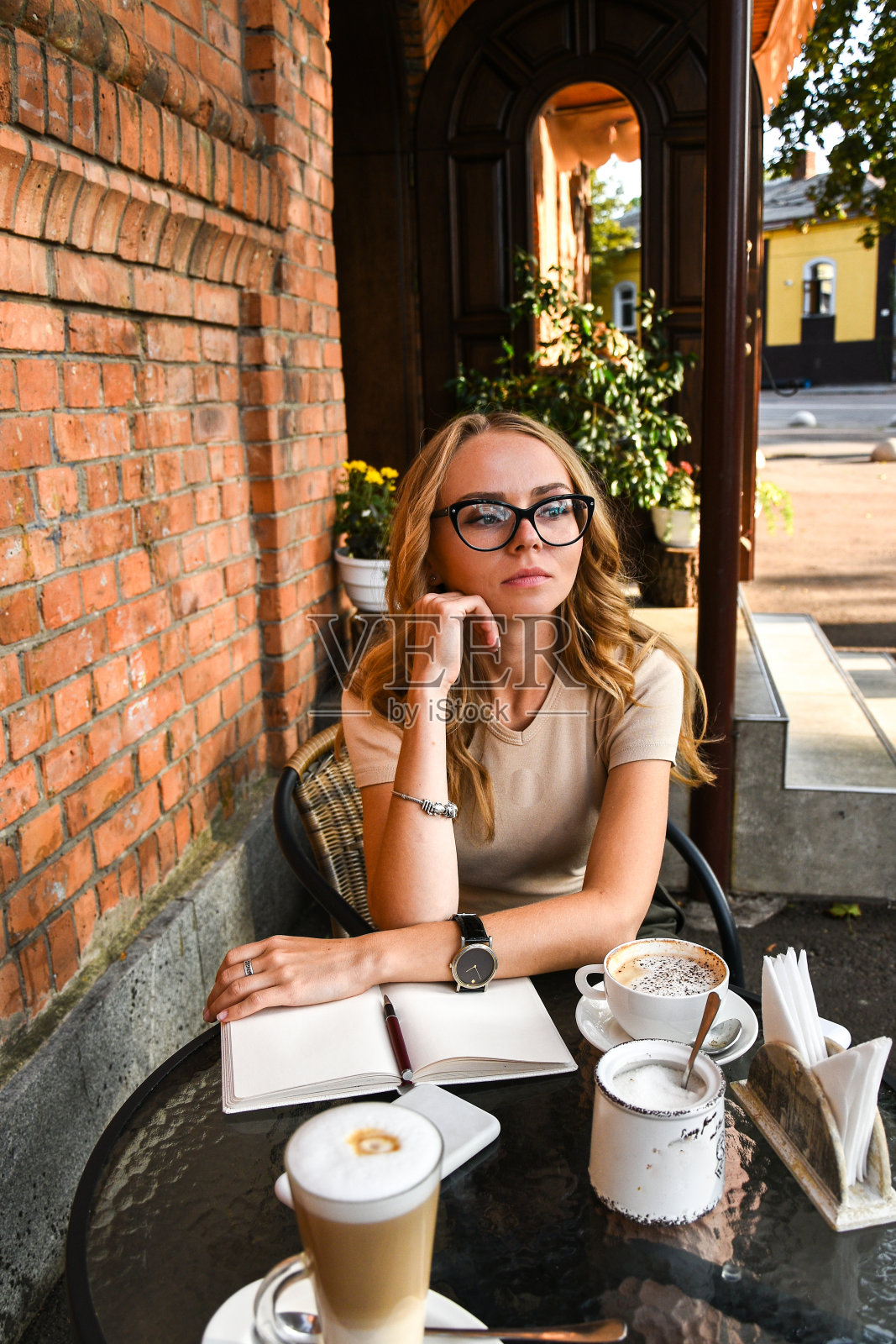 年轻女子坐在咖啡厅的砖墙背景下，在笔记本上写字。桌上有咖啡电话。在外面工作的女性自由职业者。年轻的商业女性照片摄影图片