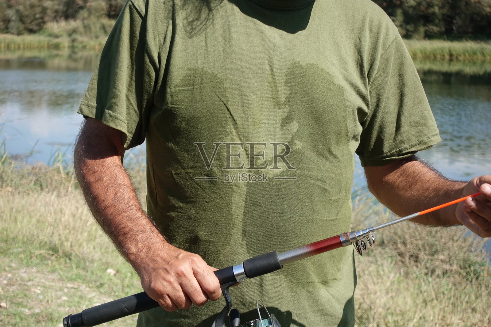 一个汗流浃背的渔夫站在湖边调整钓竿照片摄影图片