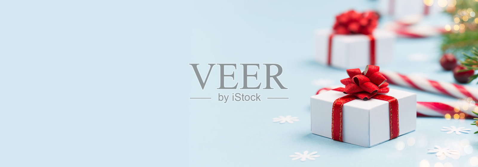 圣诞礼物，冷杉树枝，红莓和糖果拐杖在粉彩纸蓝色的背景。照片摄影图片